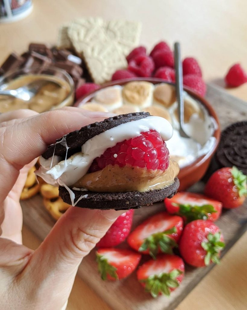 A raspberry is squished between an oreo filled with melted marshmallow and peanut butter