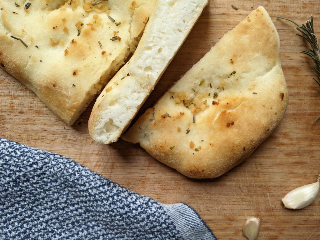 The Senza gluten free garlic and herb focaccia sliced on a chopping board. You can see the bubble distribution and fluffiness of the bread.