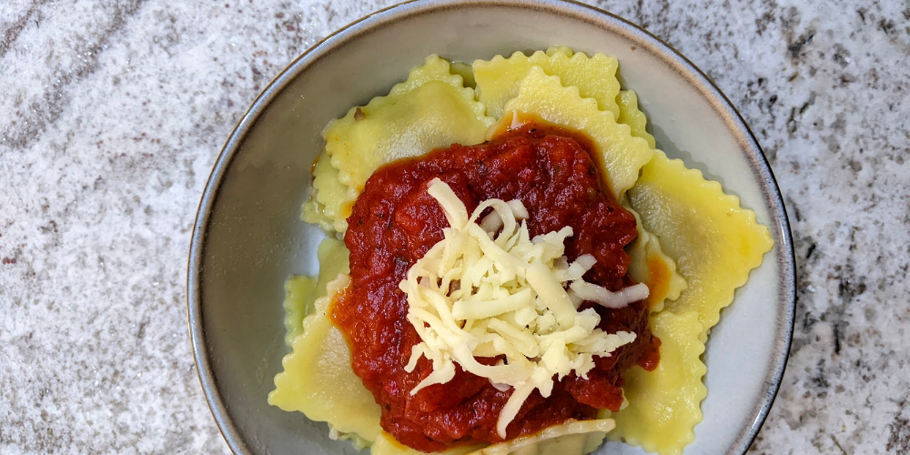 A bowl of Latina Fresh gluten free beef ravioli served with a spicy tomato sauce and grated cheese.