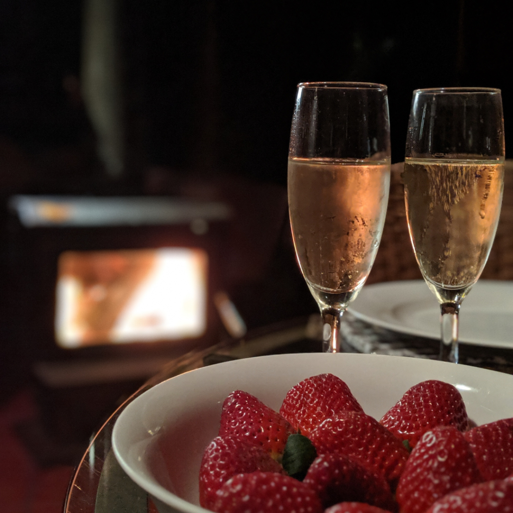 A bowl of strawberries and two glasses of champagne. In the background a fireplace can be seen. 
