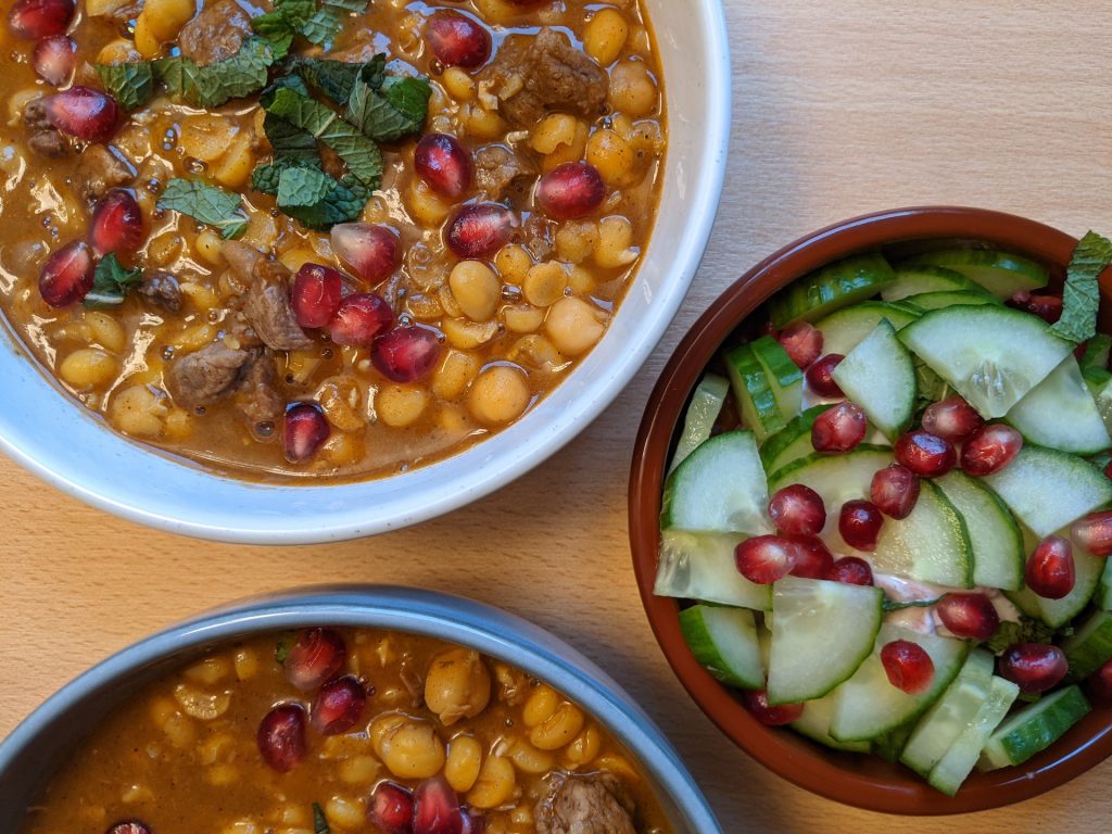 A bowl of lamb and chickpea stew and a bowl of chopped cucumber and pomegranate.