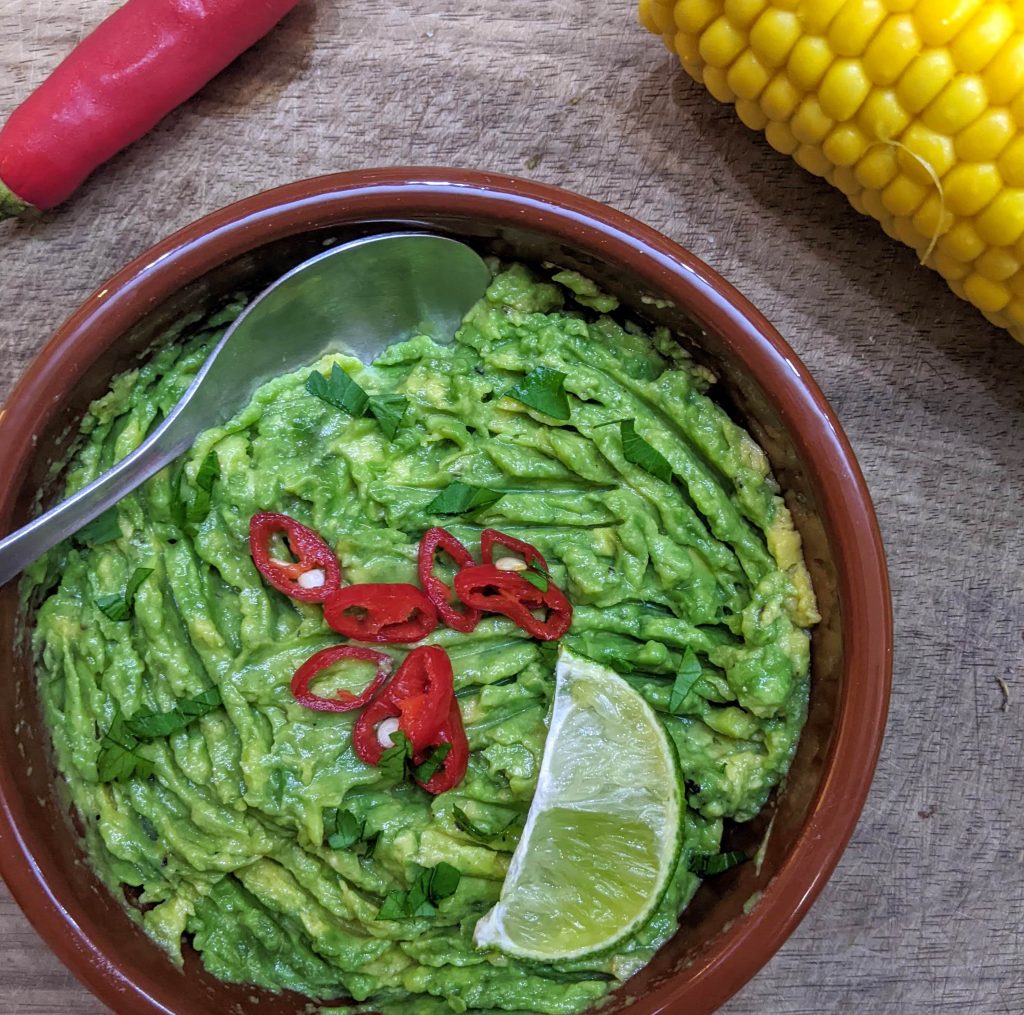 A bowl of easy guacamole garnished with sliced fresh chilli, coriander and lime. 