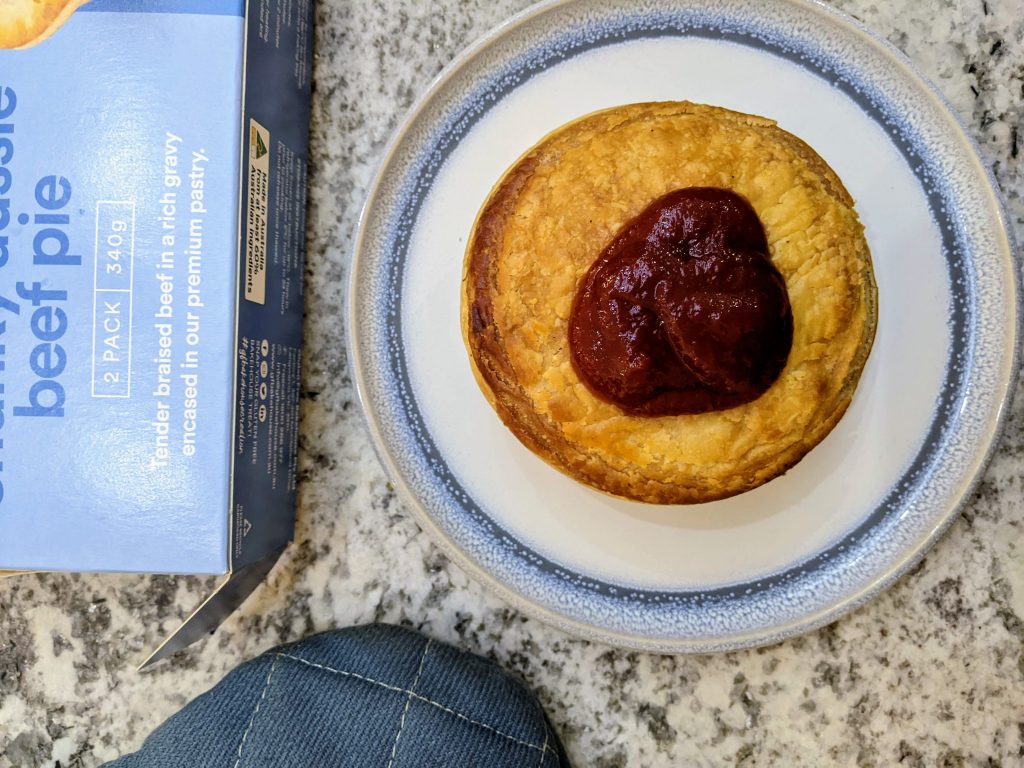 A gluten free bakehouse meat pie on a plate with a serving of tomato sauce. 