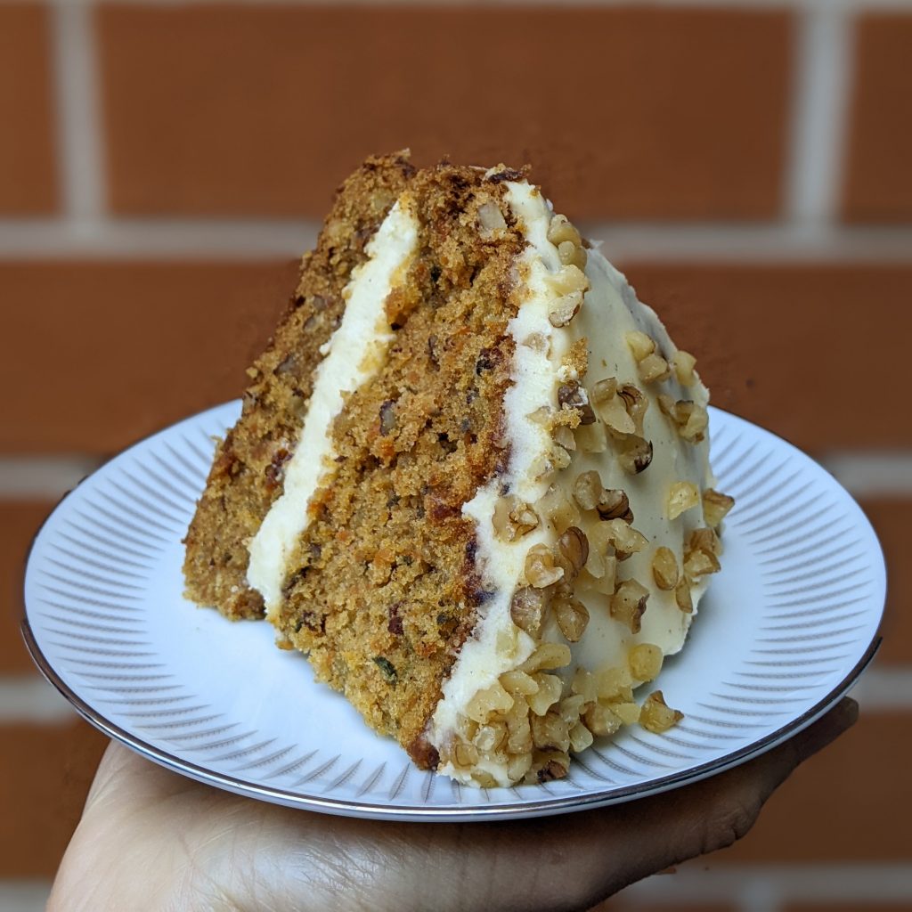 A carrot cake made of two layers of cake and two laters of icing. The top is covered in pieces of walnut.