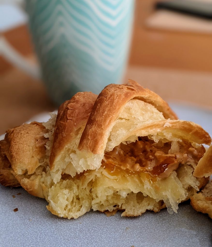A cut open croissant showing layered pastry with jam and peanut butter oozing out.