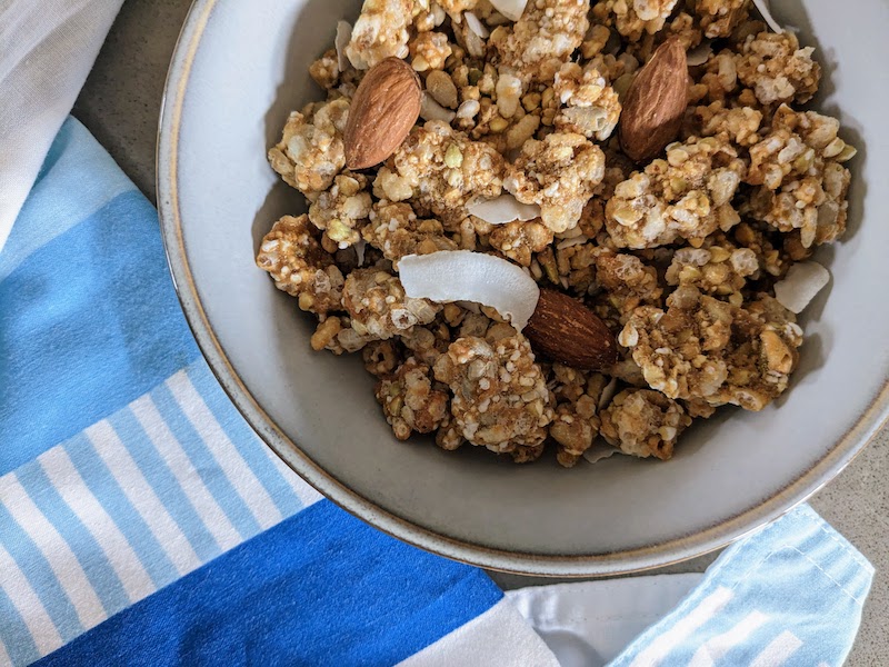 A bowl of honey almond clusters. It shows whole almonds, slivers of coconut and clusters that are bigger than the almonds. 