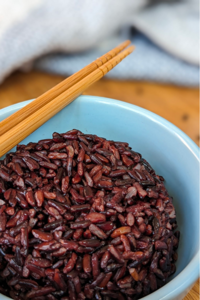 A blue bowl with cooked black rice. Wooden chopsticks are on top of the bowl.