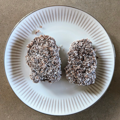 Two gluten free lamington fingers on a plate. One is significantly bigger than the other.