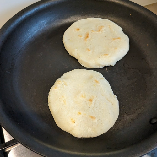 Two arepas in a frying pan. 