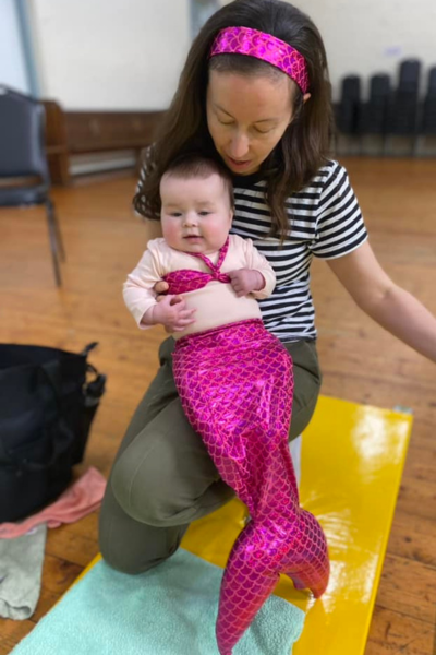 A baby wearing a pink mermaid tail and bikini being held by a woman.