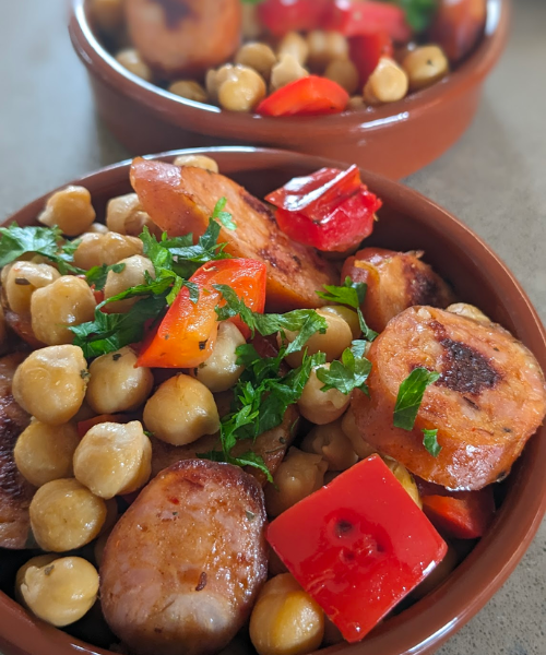 Two ramekins filled with chickpeas, chorizo slices and pieces of capsicum