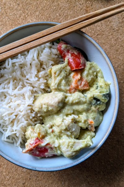 Rice and Thai green curry in a blue bowl. A pair of wooden chipsticks sit across the bowl.