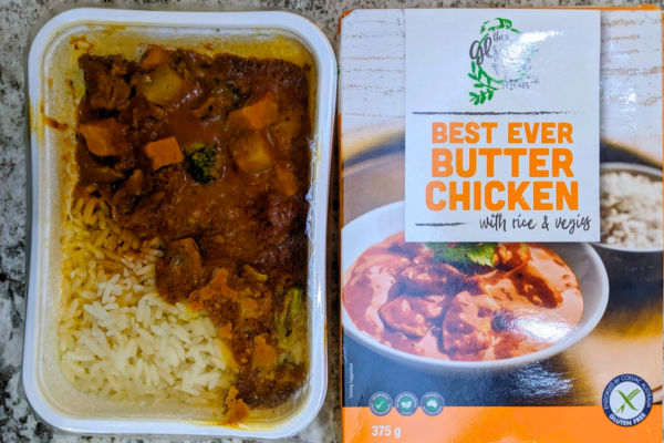 A meal tray with curry and rice next to the box of gluten free meal co best ever butter chicken.