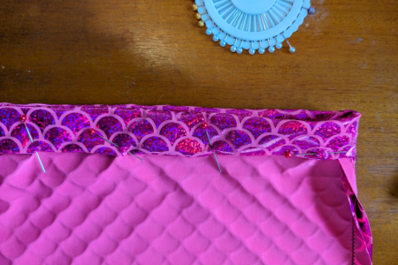 A pink fabric garment zoomed in to show a pinned hem line. 