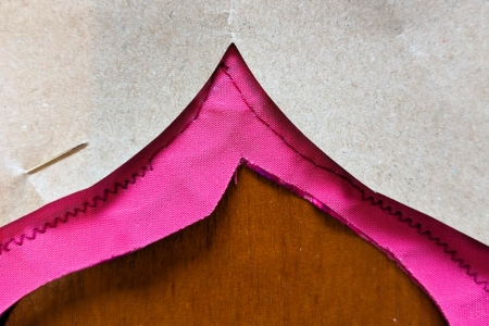 A zoomed in photo showing straight stitching on pink fabric next to a paper template.