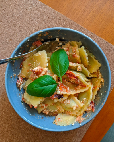 A top down view of a bowl of pasta with two basil leaves on top.
