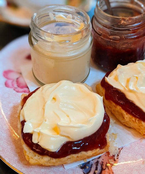 A scone with jam and cream. Behind it are jars of cream and jam.