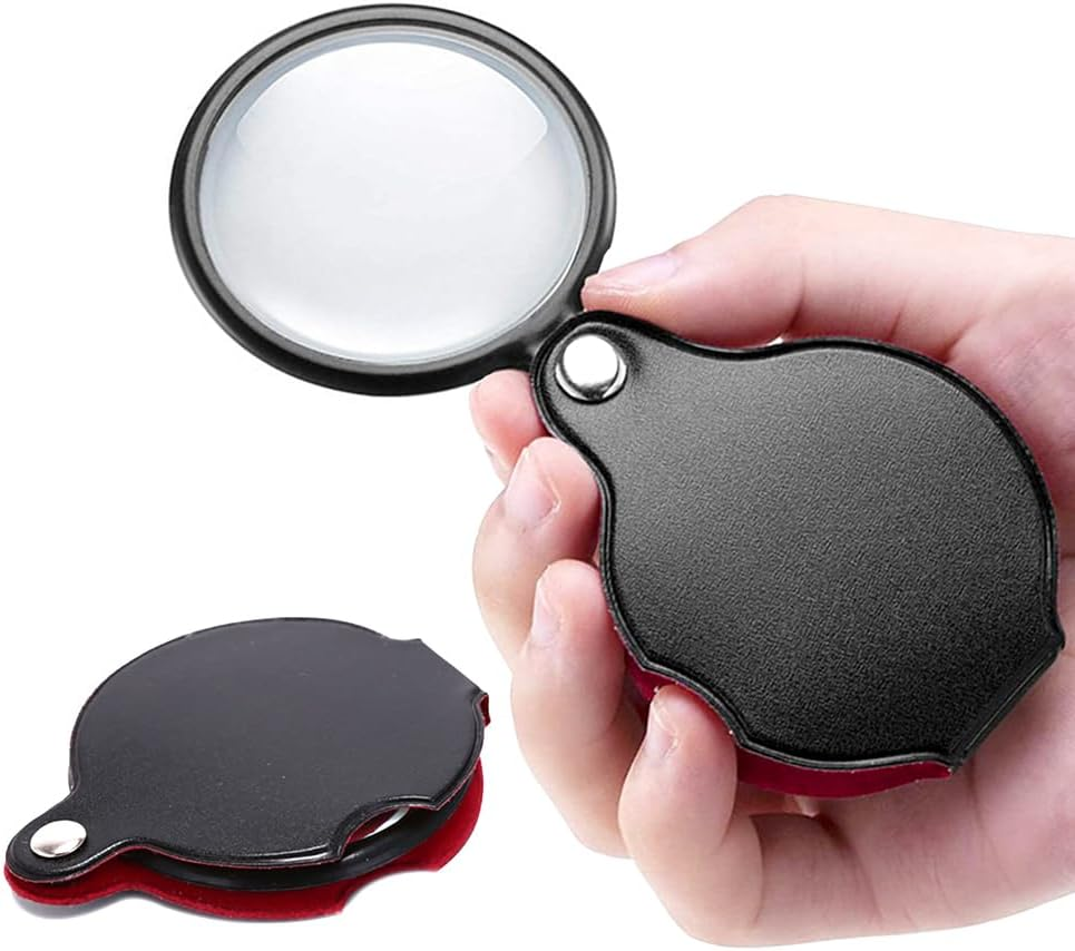 A small handheld magnifying glass in a person's right hand.