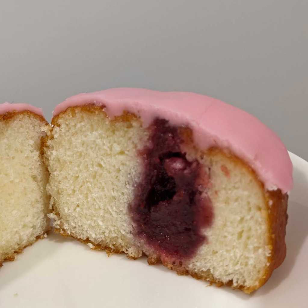 A donut with pink icing cut open to show a deep red jam inside.