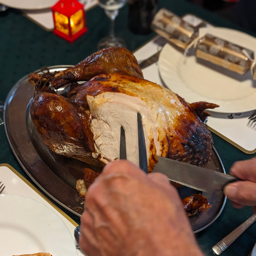 A hand in the foreground carving a turkey in the background.