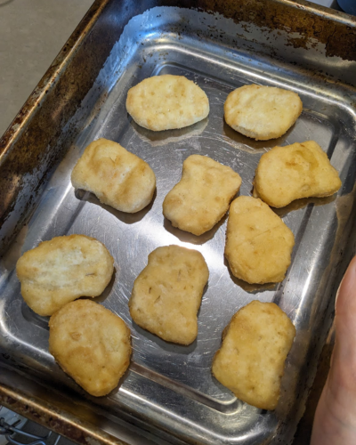 A metal baking tray with ten nuggets on it.