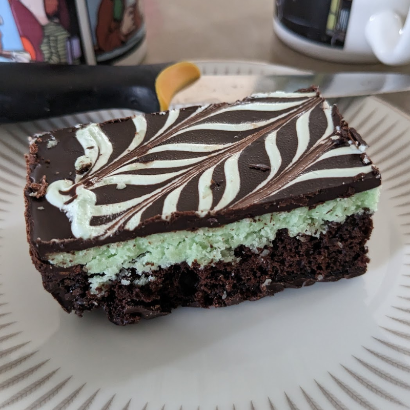 A piece of mint slice sitting on a plate with a knife behind it. 